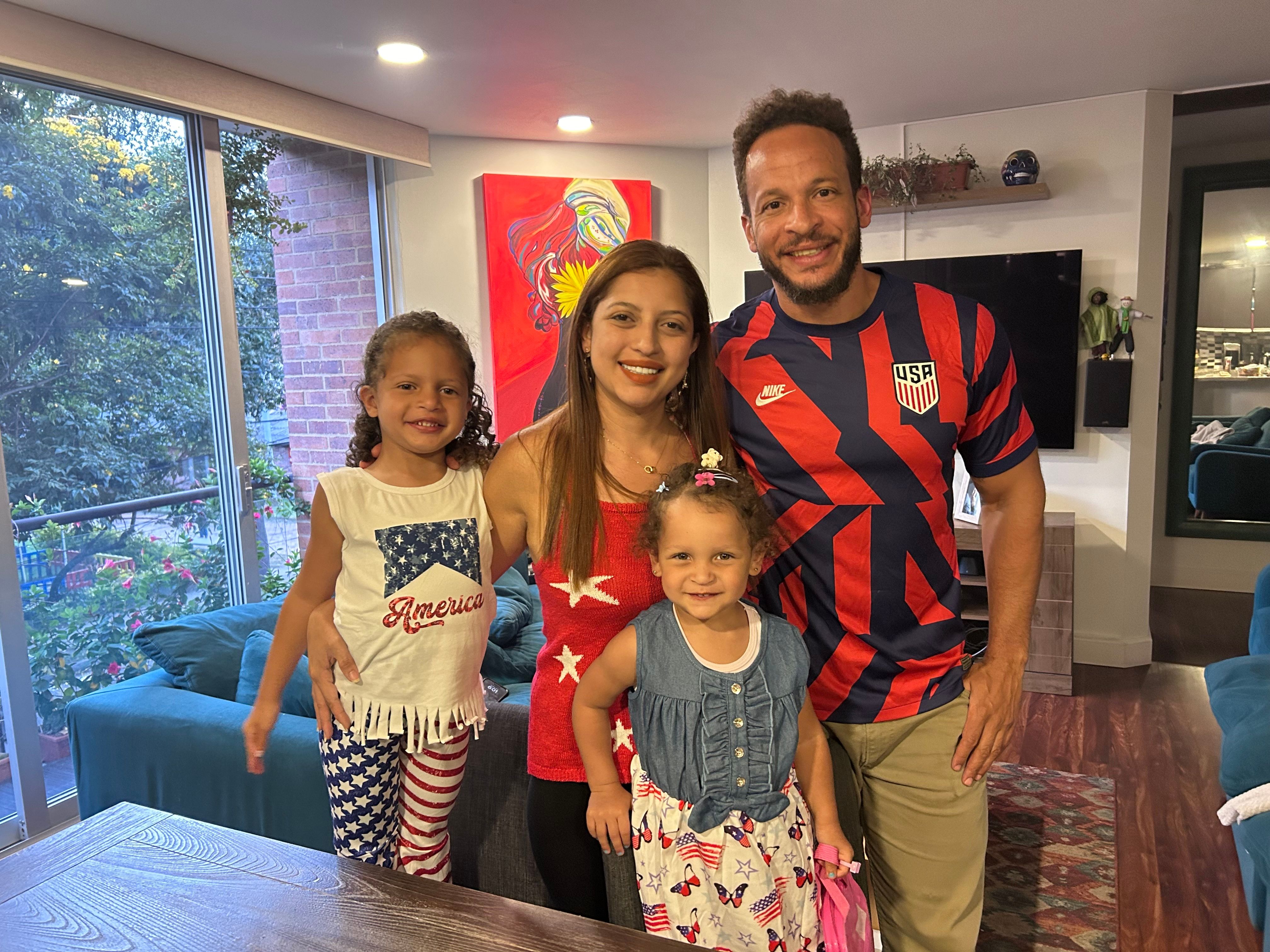 A family of four wearing American clothing inside an apartment with view. 